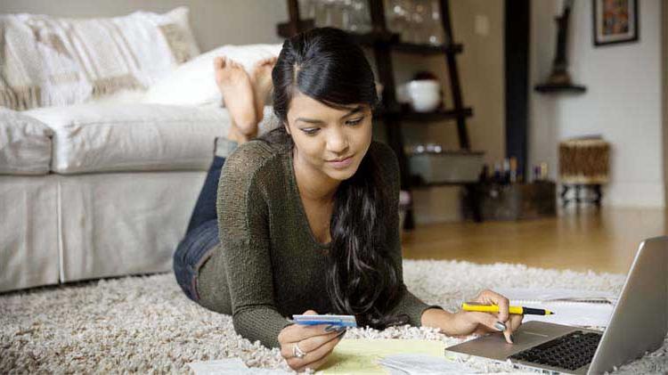 Woman laying on the floor paying bills on laptop.